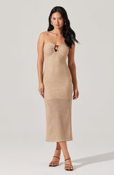A woman is wearing a strapless, beige, textured knit dress that reaches mid-calf. The dress features a gathered detail at the bust with a small decorative element in the center. She is also wearing black, strappy high-heeled sandals.